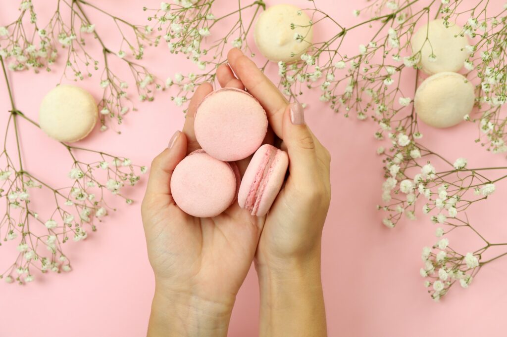 Female hands hold macaroons on pink background with macaroons and flowers