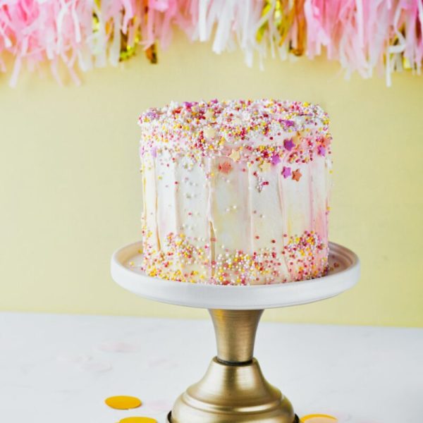 Colorful birthday cake with sprinkles on a yellow background.