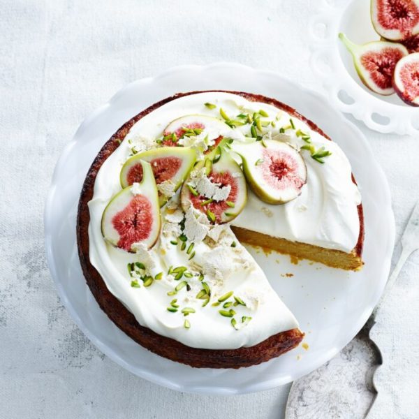 Overhead view of orange and almond cake with yoghurt cream, pistachios, figs and cake server